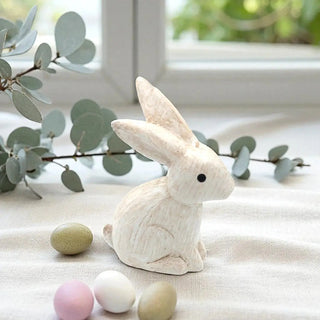 White rabbit figurine with pastel-colored eggs on a light fabric background