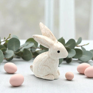 White rabbit figurine with pink eggs and eucalyptus leaves on a light background