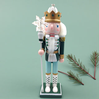 Decorative nutcracker figure with a crown and staff on a white background for a sage Christmas aesthetic