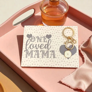 Keychain with heart design on a card labeled 'One Loved Mama' on a pink tray.