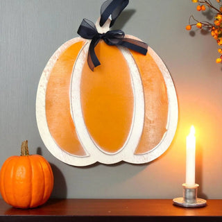 Decorative pumpkin wall art with a black ribbon, small pumpkin, and candle on a wooden surface.