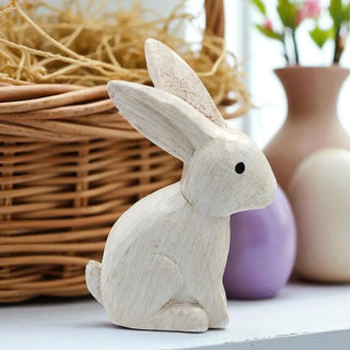 Wooden rabbit figurine on a surface with a wicker basket and vases in the background