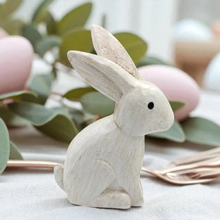 Wooden rabbit figurine on a surface with eucalyptus leaves and pink eggs in the background