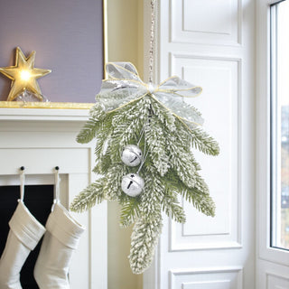 Decorative Christmas wreath with white ribbons and silver bells hanging above a fireplace with stockings.