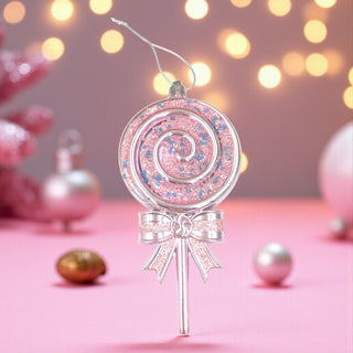 Decorative pink lollipop ornament with a bow on a pink surface with blurred lights in the background