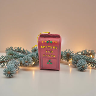 Pink mailbox ornament with 'Letters for Santa' text on a white surface with Christmas lights and branches for  a vintage Christmas Aesthetic