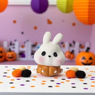 White rabbit figurine in a pumpkin outfit on a polka dot surface with Halloween decorations in the background.