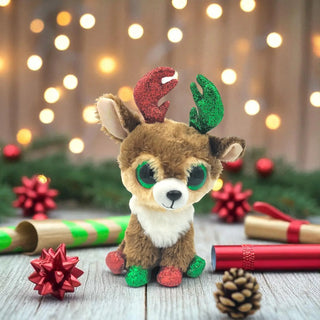 Plush reindeer toy with festive decorations on a wooden surface with blurred lights in the background