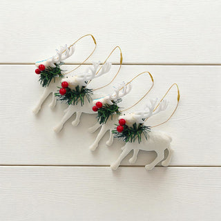 Set of white reindeer ornaments with red berries and greenery on a light wooden surface