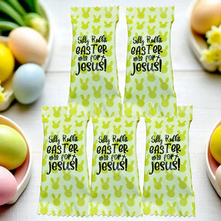 Four green and white Easter candy bags with text on a table with Easter eggs and bunnies.