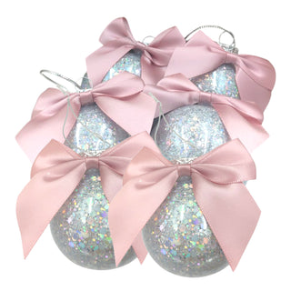 Three glittery Christmas ornaments with pink bows on a white background