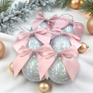 Decorative Christmas ornaments with pink bows on a white surface with gold and gold leaf accents.