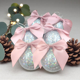 Decorative Christmas ornaments with pink bows and glittery balls, surrounded by pine cones and lights.