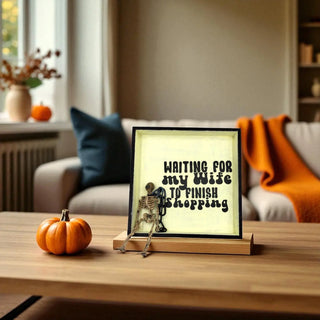 Decorative sign with skeleton and text on a table in a cozy living room.