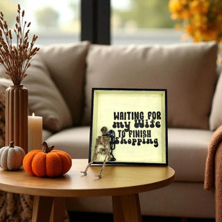 Decorative setup with a skeleton figurine, pumpkins, and a framed print on a table in a living room.
