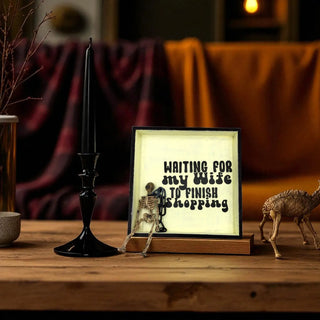 Decorative sign with skeleton and text on a wooden surface with candle and figurines.