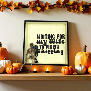 Framed print with skeleton and text on a shelf with pumpkins and candles
