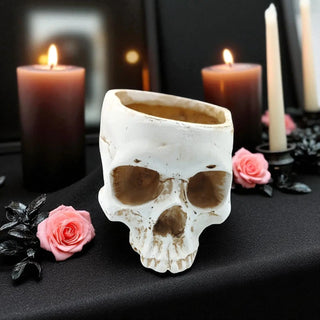 Skull-shaped candle holder with candles and roses on a dark surface