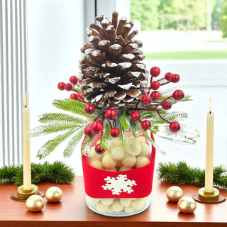 Decorative Christmas arrangement with pine cone, red berries, and gold balls on a table.
