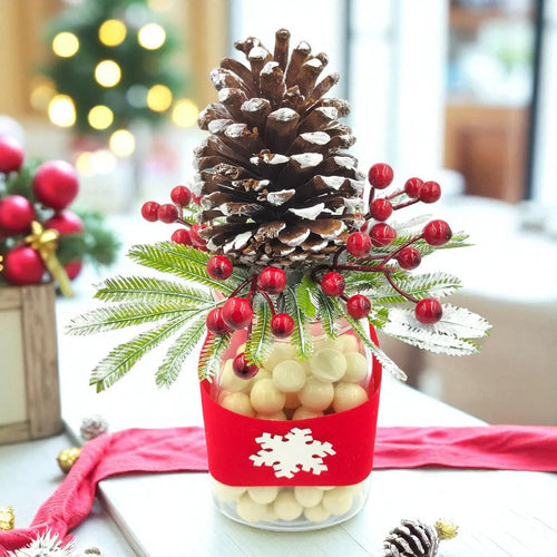 Decorative Christmas arrangement with pine cones, berries, and a red bag on a table.