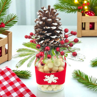 Decorative arrangement with pine cone, red berries, and greenery on a white surface.