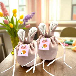 Two bunny-shaped bags with Easter tags on a table with flowers in the background