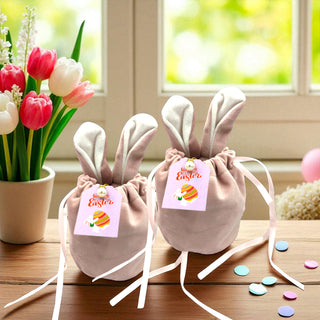 Two bunny-shaped bags with rabbit ears on a wooden surface, surrounded by tulips and confetti.