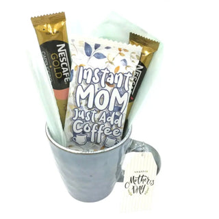 Nescafe Gold instant coffee packets with a 'Instant Mom Just Add Coffee' packet in a mug, on a white background.