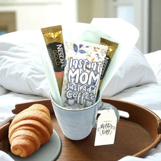 Cup with coffee packets, a croissant, and a 'Mother's Day' tag on a tray.