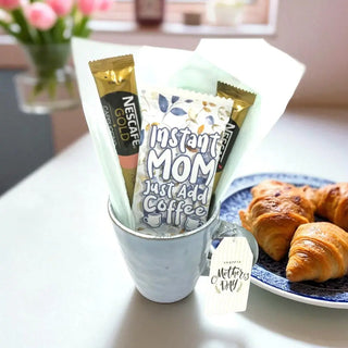 Nescafe Gold instant coffee packets in a cup with croissants on a plate.