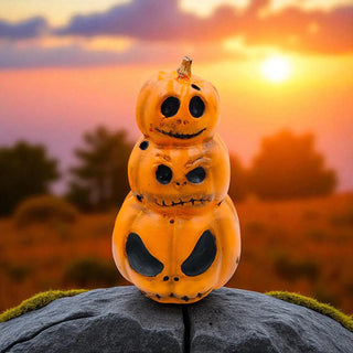 Stack of Halloween pumpkins with carved faces on a rock against a sunset sky