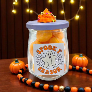 Jar labeled 'Spooky Season' filled with orange treats on a wooden surface with Halloween decorations.