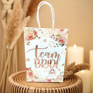 Gift bag with 'Team Bride' text and floral design on a woven surface.