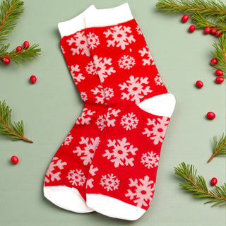 Red sock with white snowflake pattern on a light green background with Christmas decorations.