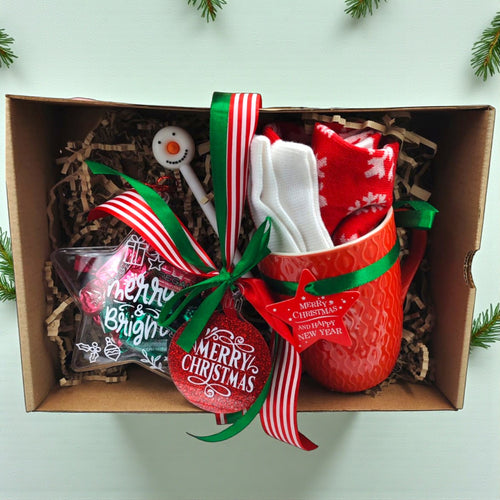 Christmas-themed gift set with red mug, candy cane, and ornament in a box.