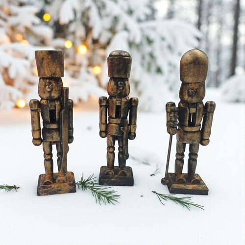 Three wooden nutcracker figurines in a snowy outdoor setting with blurred lights in the background.