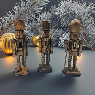 Three wooden nutcracker figurines with decorative pumpkins and branches in the background.