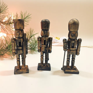 Three wooden nutcracker figurines on a white surface with a blurred Christmas tree in the background.