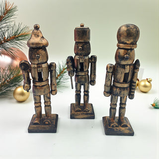 Three wooden nutcracker figurines on a white surface with Christmas decorations in the background.