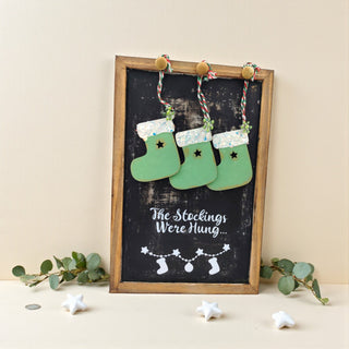 Decorative sign with green stockings and text on a blackboard background, framed in wood.
