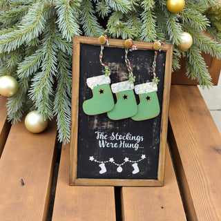 Decorative sign with stockings and Christmas tree branches on a wooden surface