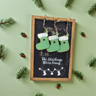 Decorative chalkboard with stockings and Christmas decorations on a green background
