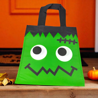 Green Halloween treat bag with a face design on a wooden surface.