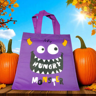 Purple tote bag with a monster design in front of pumpkins and autumn leaves.