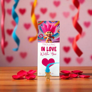 Troll doll with 'Trolling in Love with You' packaging on a wooden surface with red rose petals and heart decorations.