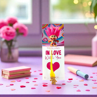 Troll doll-themed product with heart and yellow hair on a decorative surface with flowers and stationery.