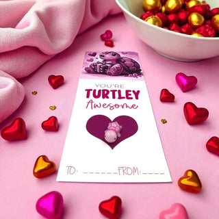 Valentine's Day card with turtle design surrounded by heart-shaped candies on a pink background