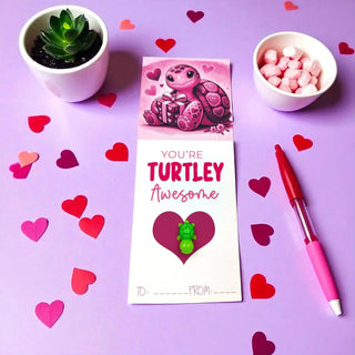Valentine's Day card with turtle design, pen, and small plants on a purple background with heart decorations.