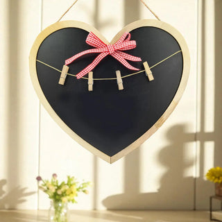 Heart-shaped blackboard with a pink bow and clothespins in a room with sunlight streaming through curtains.
