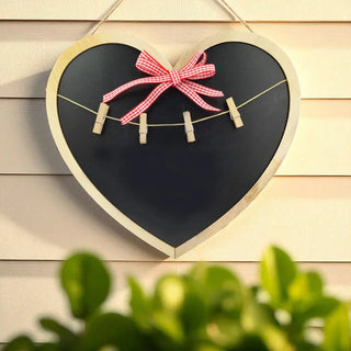 Heart-shaped blackboard with a pink bow and clothespins on a wooden wall.